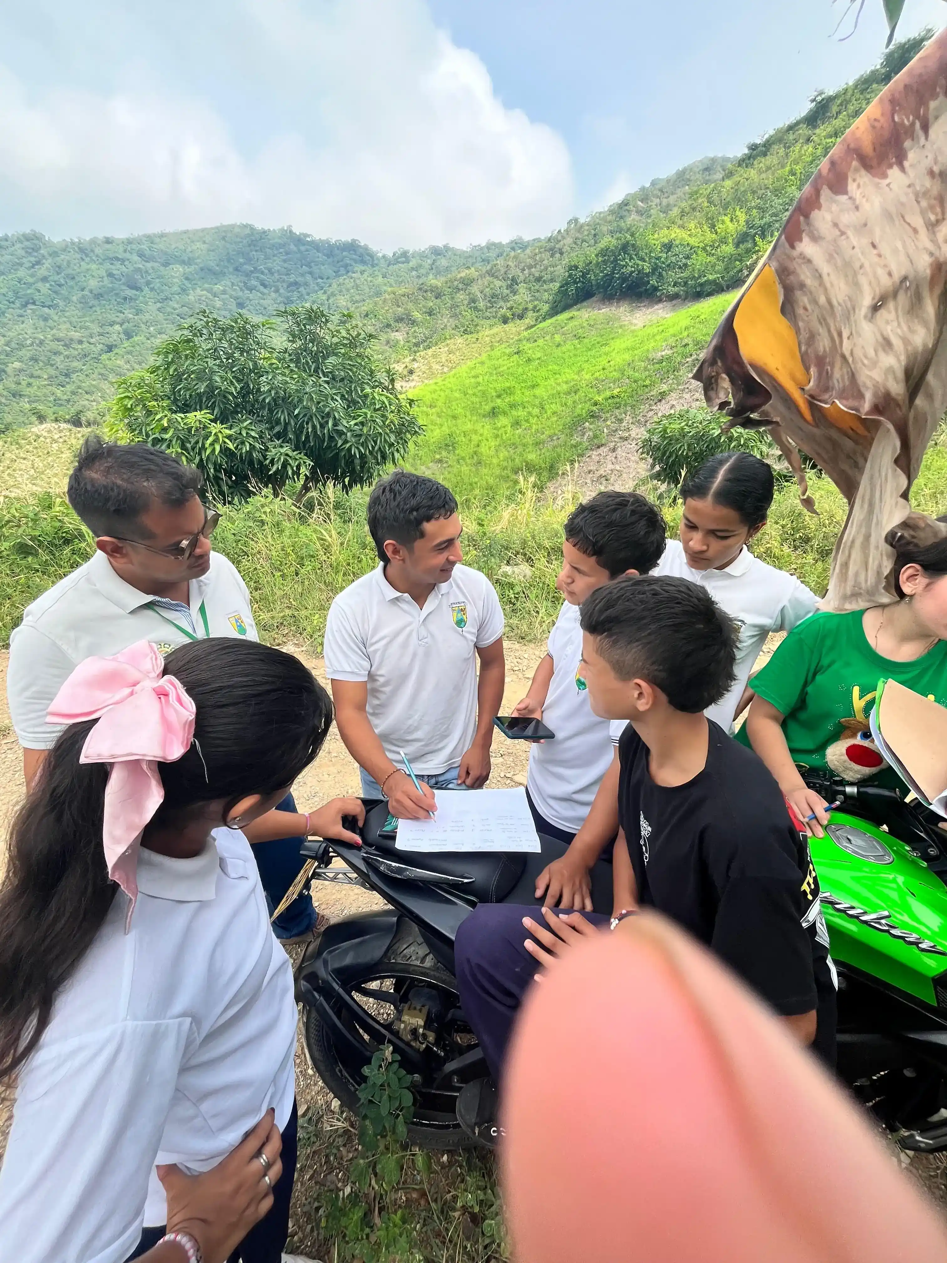 Grupo de estudiantes y acompañantes registrando datos sobre el asiento de una moto, con cerros verdes al fondo